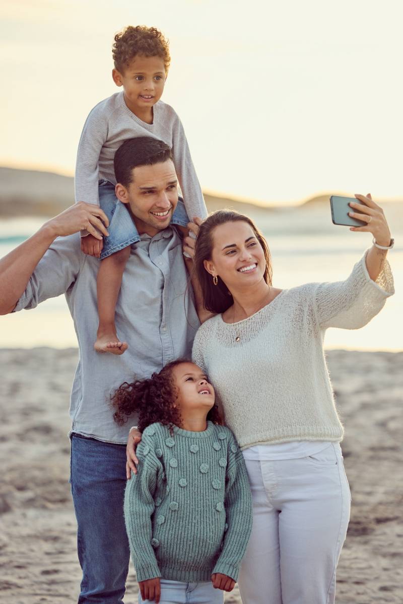 Happy cheerful mixed race family smiling for a selfie spending time at the beach together. Hispanic